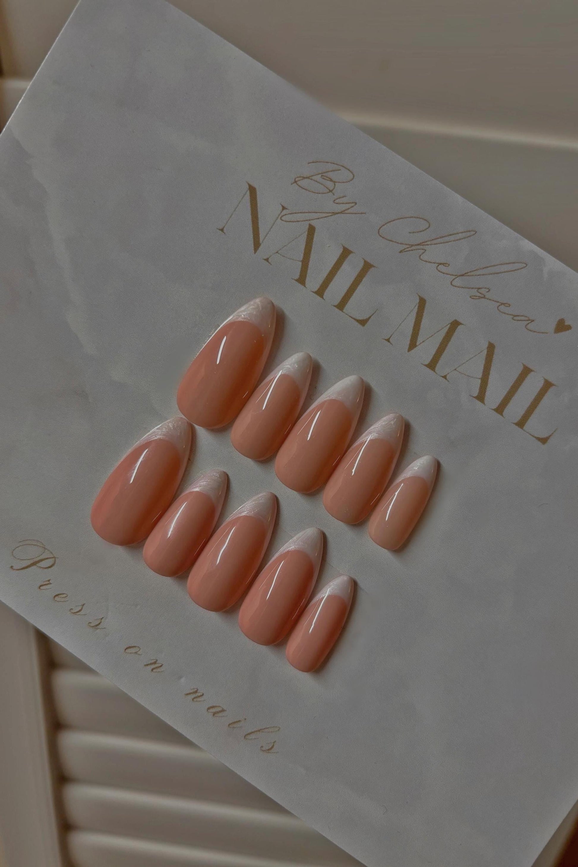 Set of nude almond-shaped press-on nails with white V-cut French tips on branded Nail Mail card